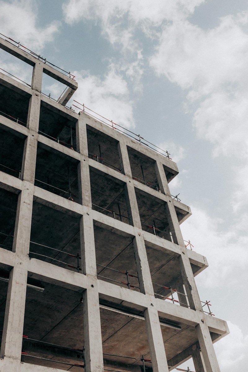Rohbau aus Betonstützen und Decken mit Absturzsicherung, von unten gesehen vor bewölktem Himmel