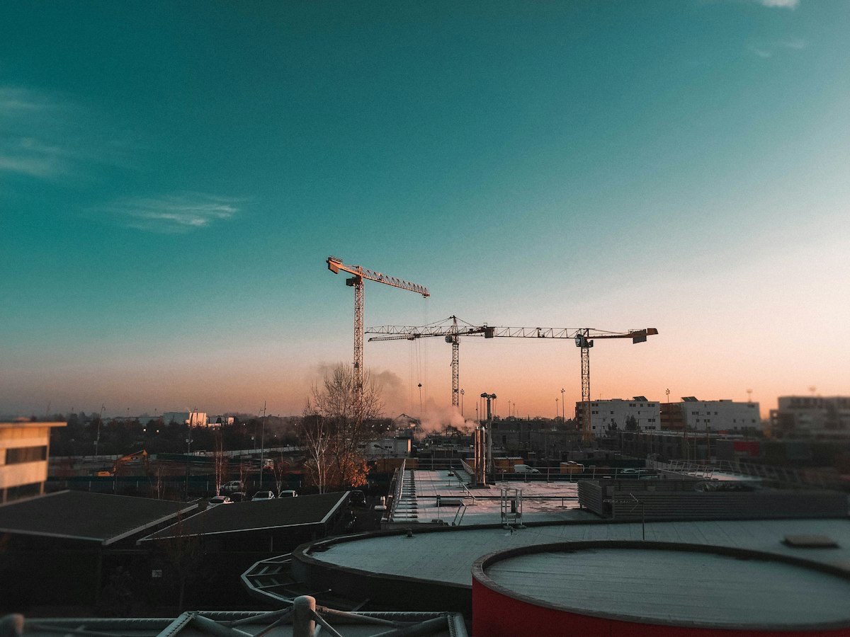 Drei Turmdrehkräne über einer Baustelle im Abendlicht