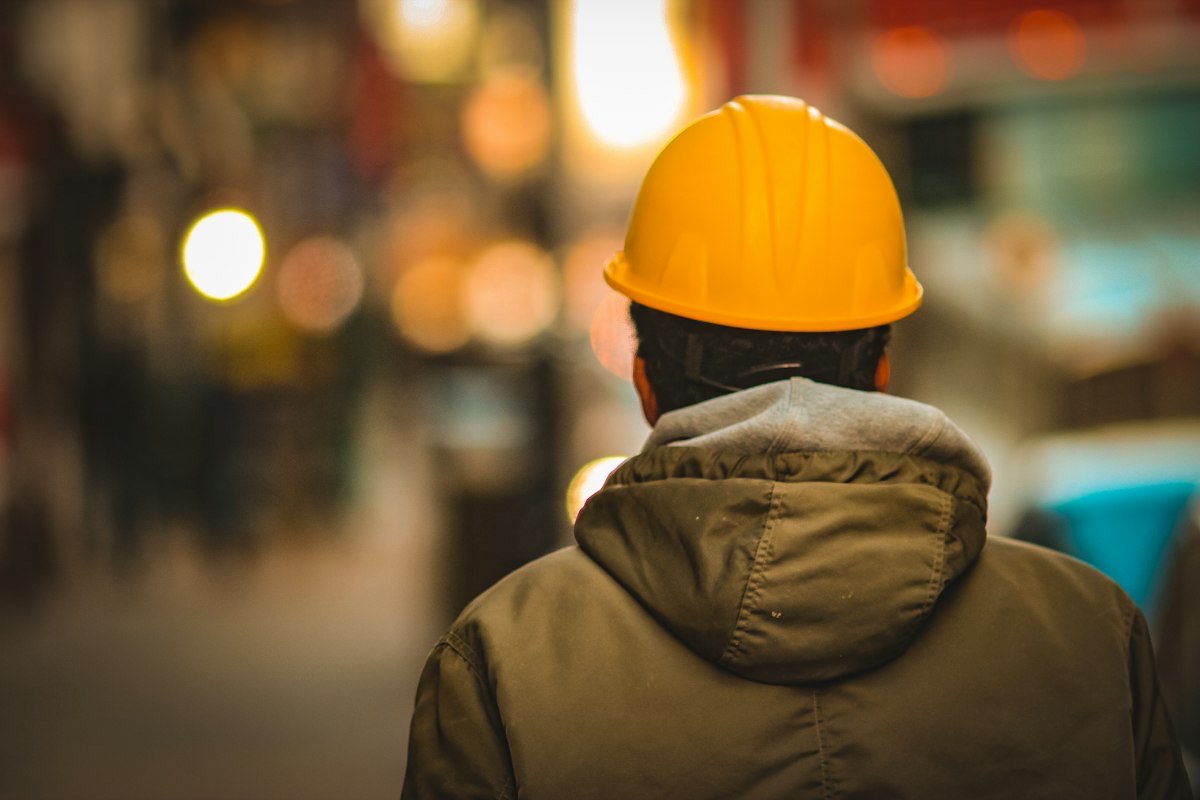 Bauarbeiter mit gelbem Helm, von hinten gesehen, im Abendlicht einer Straße