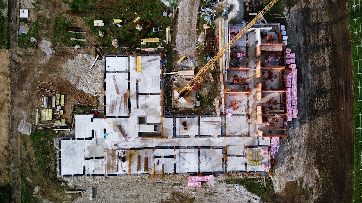 Baustelle von oben mit Bodenplatte, ersten Wänden und einem Turmdrehkran